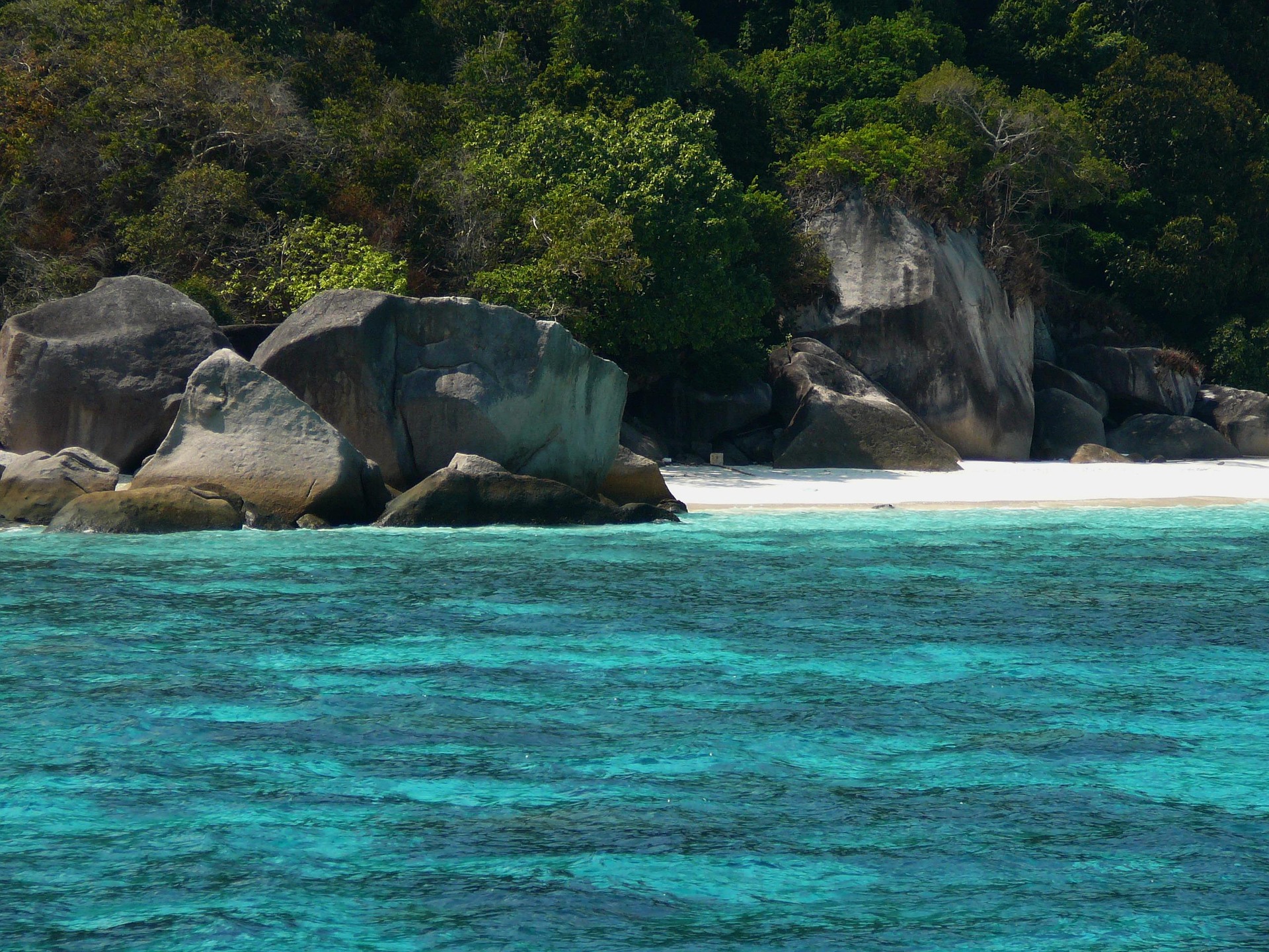 Clear water beside a white sand beach and granite rocks in the Similan Islands